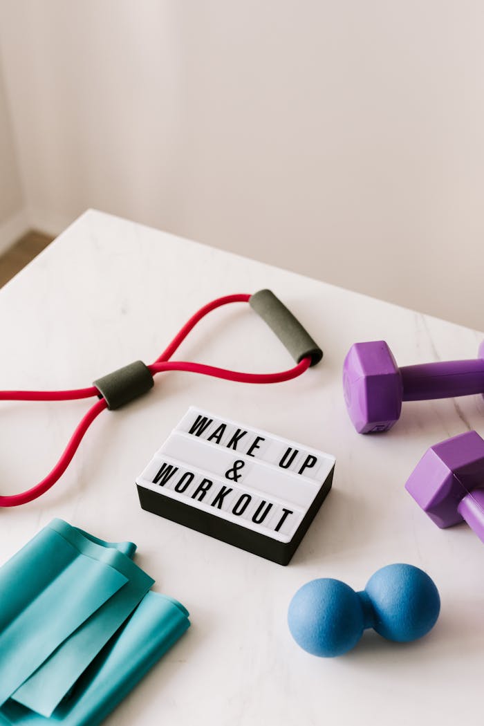 about-us From above composition of dumbbells and massage double ball and tape and tubular expanders surrounding light box with wake up and workout words placed on white surface of table